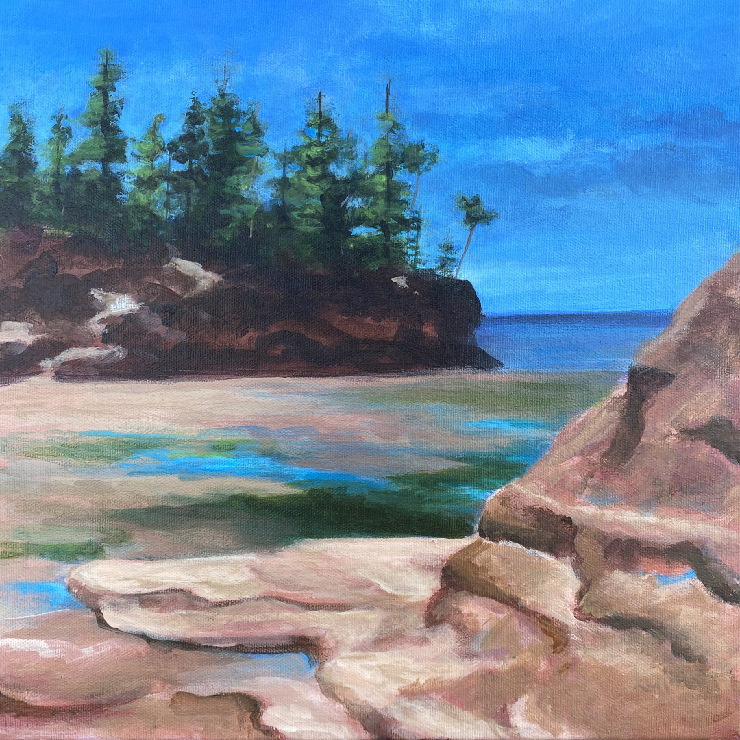 Reddish cliffs are set against the blue sky and water of the low tide.